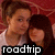 Two people in close proximity with one person's head resting on the other's shoulder, set against a red patterned background and overlaid with 'roadtrip' text.