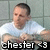 Pixelated image of a person in a white shirt with short dark hair, standing against a light gray grid-patterned background, with text at the bottom reading 'chester <33'.