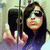 Pixelated image of a person with long dark hair holding a microphone, wearing a dark top, against a light background with vertical lines.
