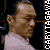 Pixelated profile view of a person with light brown skin, short brown hair, and a white shirt against a dark background with vertical white text on the right.