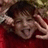 Pixelated static image of a person with dark hair wearing a red garment, hands raised near the head in a gesture, against a blurred background.