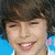 A pixelated close-up of a person with dark hair, light skin, and visible teeth in a smiling expression against a blue background.