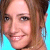 Pixelated close-up of a smiling person with light brown hair against a bright blue background, rendered in low-resolution 256x256 pixels.