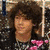 A person with curly brown hair appears in three distinct poses: upper-left with a dark patterned background, upper-right against a plain white backdrop, and lower-left with a light background featuring pink shapes.