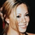 Pixelated close-up of a person with light brown hair tied up, smiling, against a dark background.