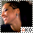A person with dark hair in a side ponytail, wearing a black top and small earrings, smiling in profile view with text 'AKO' below.