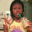 A person in a yellow shirt with purple and orange patterns holds a white phone, takes a mirror selfie, has dark hair, and uses a green toothbrush.