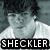 Pixelated grayscale image of a person with dark hair wearing a light-colored shirt, overlaid with bold text reading 'SHECKLER' in white letters on black background.