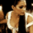 Pixelated static image of a person in motion with light brown hair, wearing a white sleeveless top and dark pants against black background.