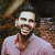 Pixelated static image of a person with short dark hair wearing a light-colored shirt, smiling broadly against a blurred background.