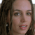 Pixelated close-up of a person with long brown hair, light skin, and visible teeth in a neutral expression.