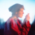 Pixelated profile of a person with short dark hair wearing a red garment, hand raised near face against light blue gradient background.