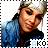 Pixelated image of a person with light brown skin wearing a blue denim jacket and white headband, smiling with eyes partially closed.