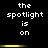 Black background with white pixelated text reading 'the spotlight is on' in two , separated by a yellow horizontal bar that changes brightness across frames
