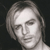 Pixelated grayscale portrait of a person with shoulder-length hair, neutral expression, and dark background.