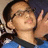 A person wearing glasses and a blue shirt with dark collar makes a peace sign, visible in four -aligned