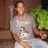 A pixelated image shows a person in a light gray t-shirt with a white and yellow graphic, standing indoors near green foliage.