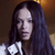 A pixelated close-up of a person with long dark hair wearing a white and black garment against a brown background.