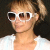 A pixelated close-up of a person wearing white-framed sunglasses and a light-colored top against a dark background.