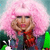 Pixelated image of a person with pink hair holding a microphone, wearing a red and blue outfit against a gradient background.