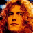 Pixelated close-up of a person with curly red hair and warm-toned skin, rendered in orange-red hues against dark background elements.