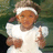 Pixelated image of a person with light brown hair wearing a white headband and white short-sleeve shirt, making a peace sign with right hand and holding left hand near head.