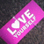 A pink rectangular icon with white text and a heart symbol, tilted diagonally against a dark pixelated background.