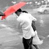 A person in a white shirt and dark pants holds a red umbrella while walking in the rain, with a blurred background of cars and streetlights.
