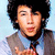 Pixelated image of a person with dark hair wearing a light blue shirt and gray jacket against a pale blue background.