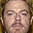 A pixelated close-up of a person's face with closed eyes, light skin tone, and visible facial features including eyebrows, nose, mouth, and ears against a dark background.