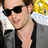 Pixelated close-up of a person wearing dark sunglasses and a black sleeveless top, with brown hair visible on the right side.