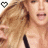 A pixelated image of a person with long blonde hair wearing a black top, featuring a heart symbol in the corner that changes color.