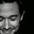 Black-and-white grayscale image of a person's face with closed eyes and a slight smile, displayed in a with visible pixelation