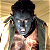 Pixelated static image of a humanoid figure with dark hair, gray face, and light skin tones against a yellowish background.