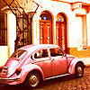 A pink Volkswagen Beetle parked on a cobblestone street in front of a building with arched red doors and a tree with bare branches.