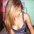 Pixelated image of a person with long brown hair wearing a dark blue sleeveless top, standing against a light blue background with a pink object on the left.