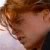 A pixelated close-up of a person's face with brown hair and light skin, showing partial facial features against a blurred background.