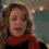 A person with curly brown hair wears a red scarf and black top, shown in four sequential poses with changing facial expressions and head positions against a blurred indoor background.
