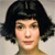 Pixelated portrait of a person with short dark hair against a light background, showing facial features and shoulders.