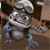 Animated metallic robot with chef's hat, shifting from side to side with arms crossed to arms extended, against blurred background.