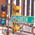 Pixelated street scene with teal sign reading 'BOSTON' over yellow and brown structures, orange and blue circular elements on left, vertical striped background.