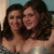 Two women with long dark hair smiling closely together in a static image.