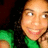 A pixelated close-up of a person with light skin wearing a green top, smiling broadly against a dark background.