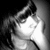 Black-and-white image of a person with dark hair resting their chin on a hand, wearing a light-colored top, with a blurred background.