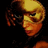 Pixelated close-up of a person with light brown hair and dark eyes, wearing red lipstick against a black background.
