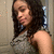 A pixelated static image shows a person with long dark hair wearing a sleeveless patterned top against a neutral background.
