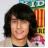 Pixelated static image of a person with dark shoulder-length hair, light skin tone, and a neutral expression against a blurred background.