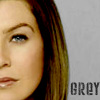 Close-up of a person's face with brown hair, blue eyes, and light skin, with the word 'GREY' in pixelated text on a light gray background.