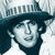 Pixelated image of a person wearing a dark wide-brimmed hat and dark clothing, with a light background showing faint vertical lines.