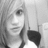 Grayscale pixelated portrait of a person with light hair and dark clothing, cropped to show upper body against plain background.